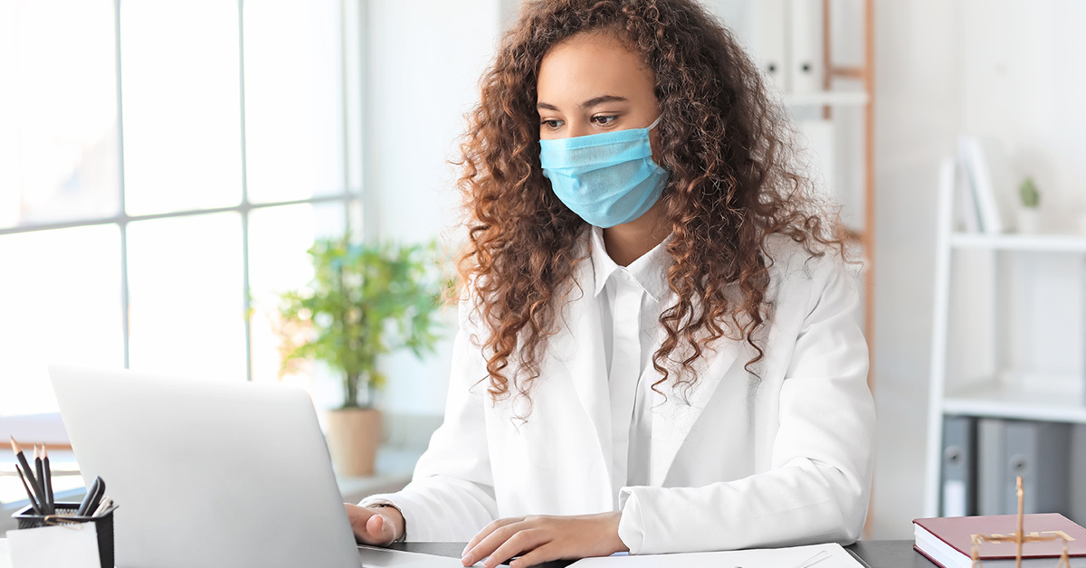 Professional woman on a laptop, wearing a face mask.